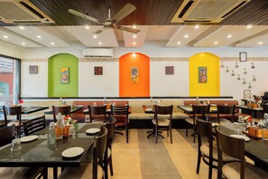 A restaurant with multiple tables and booths, ceiling fans, and wall-mounted air conditioning units. - Kyriad Prestige Calangute Goa by Othpl (Calangute)