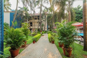 A pathway lined with potted plants leading to a building with balconies and a pool area. - Kyriad Prestige Calangute Goa by Othpl (Calangute)