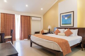 A hotel room with a large bed, a desk, a chair, and a painting on the wall. - Kyriad Prestige Calangute Goa by Othpl (Calangute)