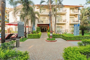 A hotel entrance with a paved pathway, palm trees, and a signboard. - Kyriad Prestige Calangute Goa by Othpl (Calangute)