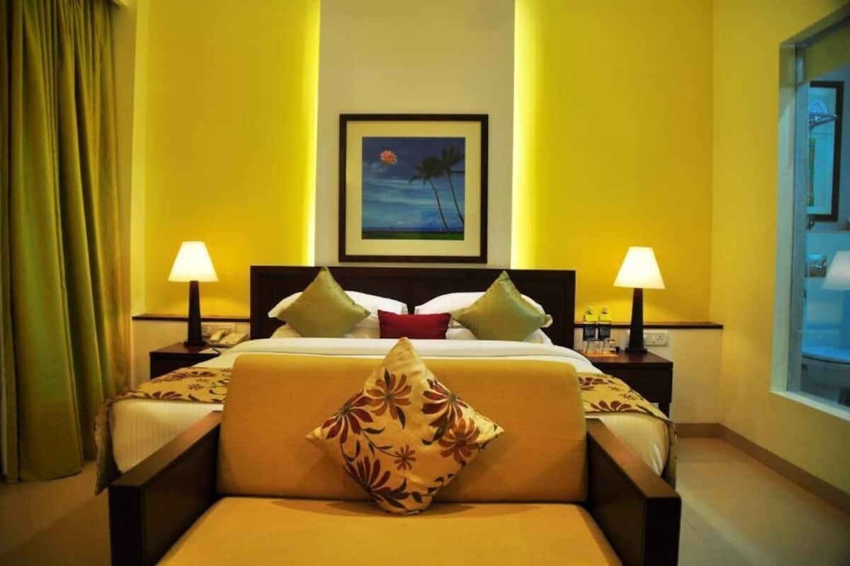 Una habitación de hotel con una cama, dos lámparas de noche, un cuadro en la pared y una ventana.