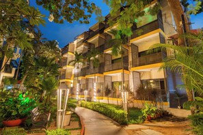 Un hotel de varios pisos con balcones, un camino y plantas en macetas.