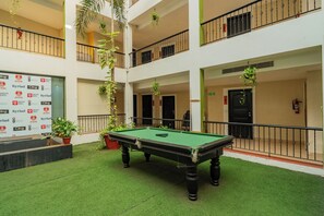 A pool table in a multi-level atrium with balconies and hanging plants. - Kyriad Prestige Calangute Goa by Othpl (Calangute)
