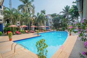 A swimming pool with lounge chairs and umbrellas, surrounded by palm trees and potted plants. - Kyriad Prestige Calangute Goa by Othpl (Calangute)