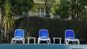 A poolside area with three lounge chairs, a tiled pool, and a hedge in the background. - Wairakei Resort Taupo (Wairakei)