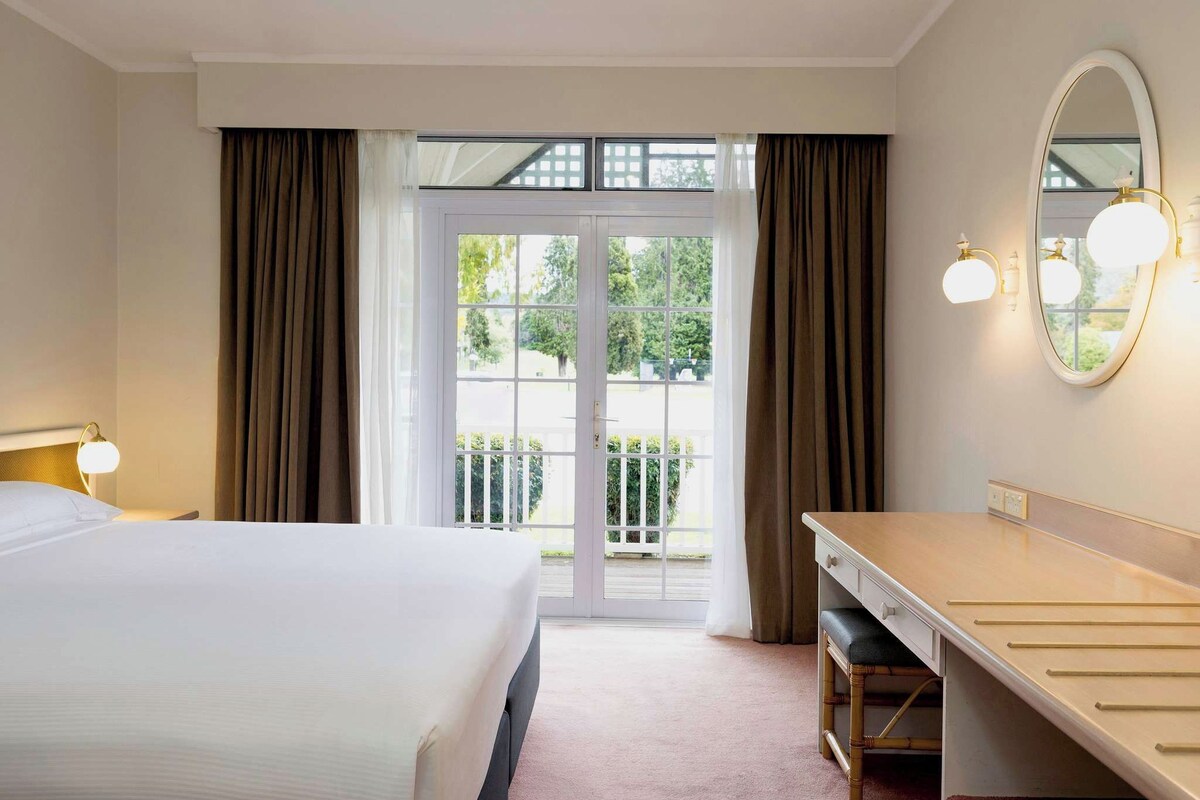 Una habitación de hotel con cama, escritorio, espejo y vistas al exterior.