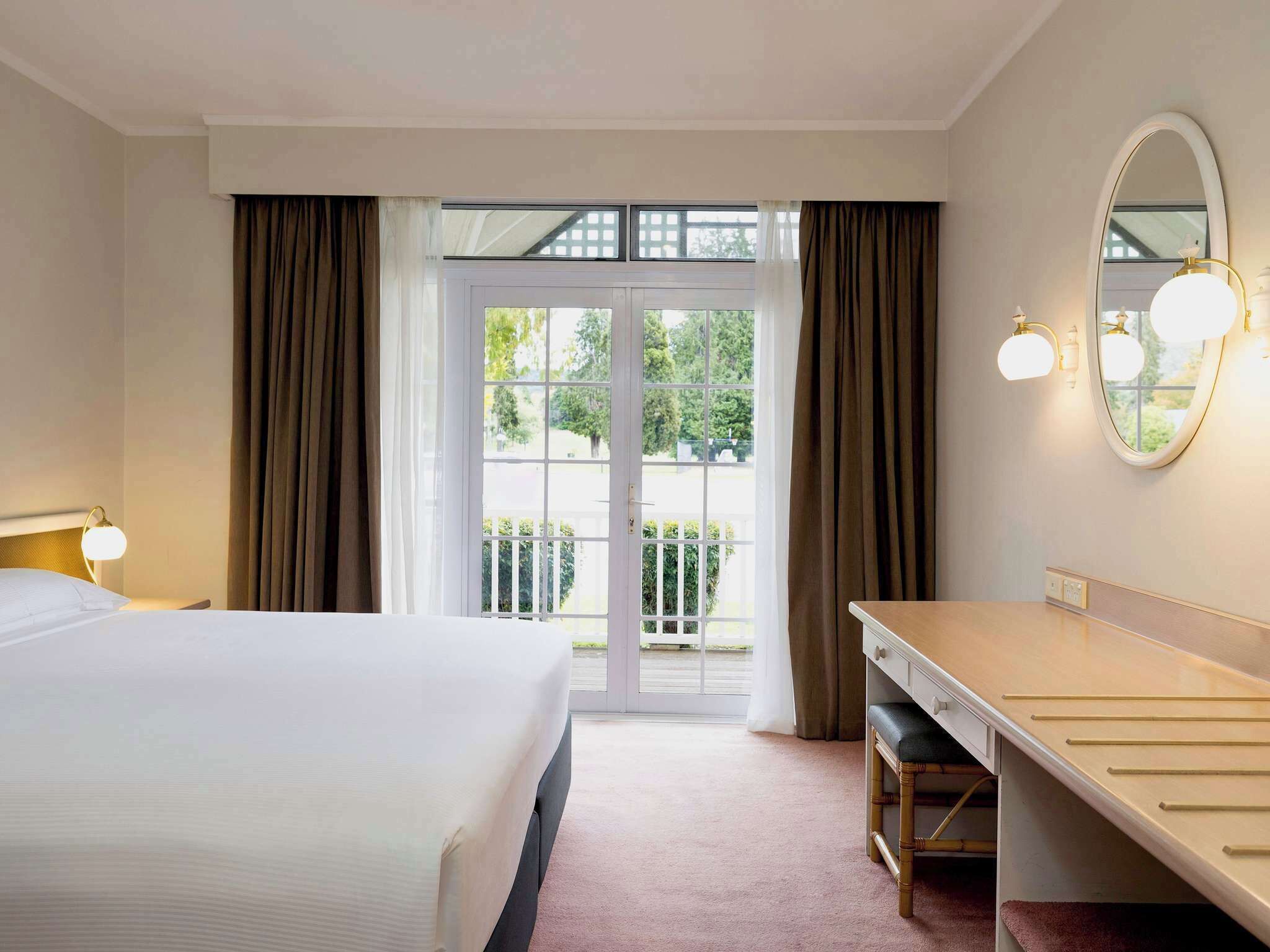 Ein Hotelzimmer mit Bett, Schreibtisch, Spiegel und Blick ins Freie.