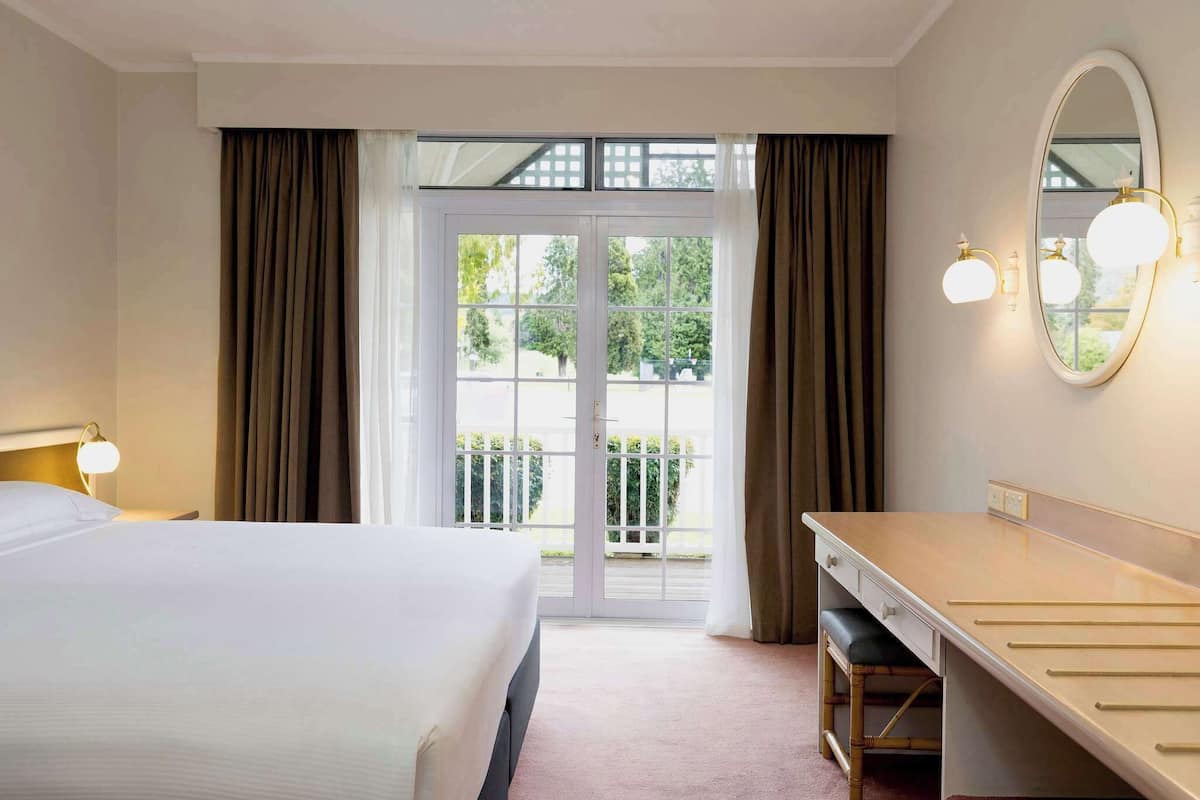 Una habitación de hotel con cama, escritorio, espejo y vistas al exterior.
