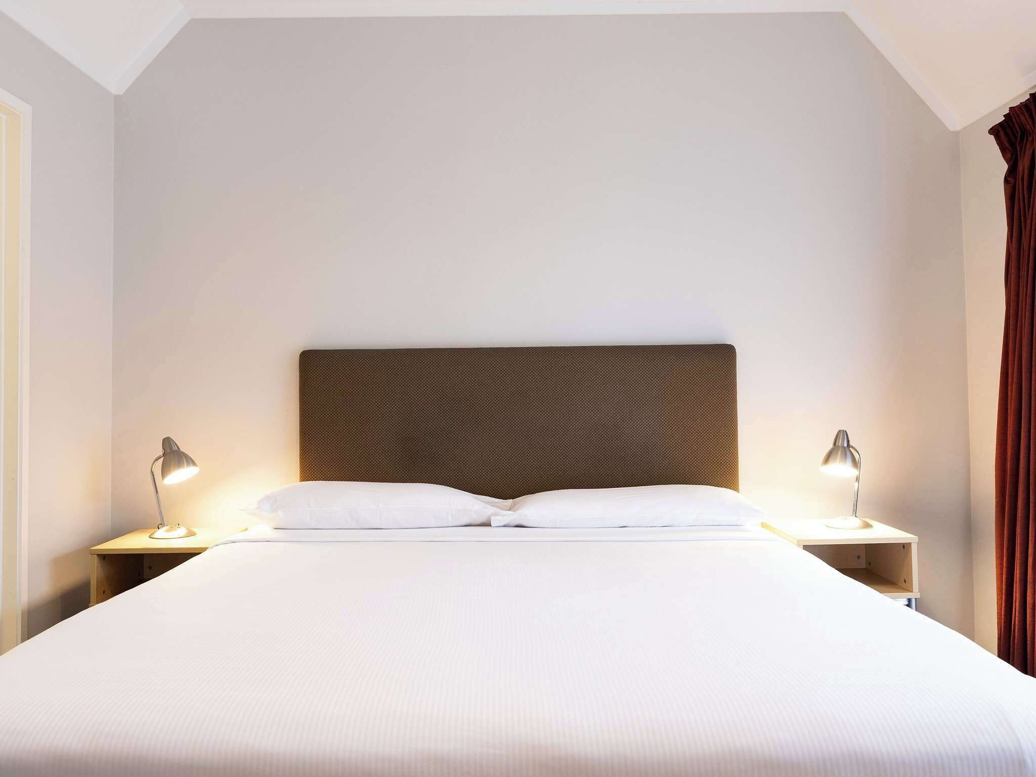 Ein ordentlich bezogenes Bett mit Kopfteil, zwei Nachttischlampen und einem Holznachttisch.