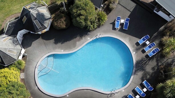An aerial view of a swimming pool with a curved edge, surrounded by lounge chairs and greenery.