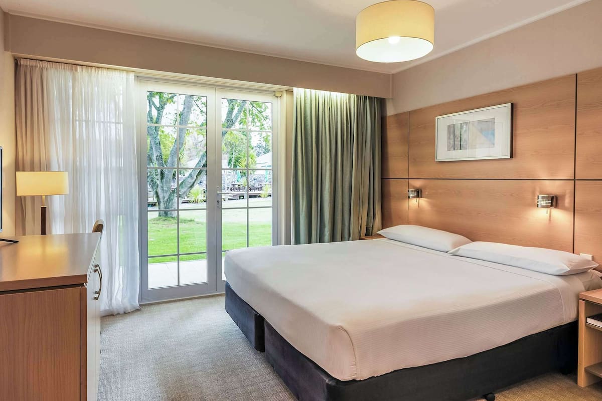 Habitación de hotel con cama, escritorio, lámpara, un cuadro en la pared y vistas por la ventana.