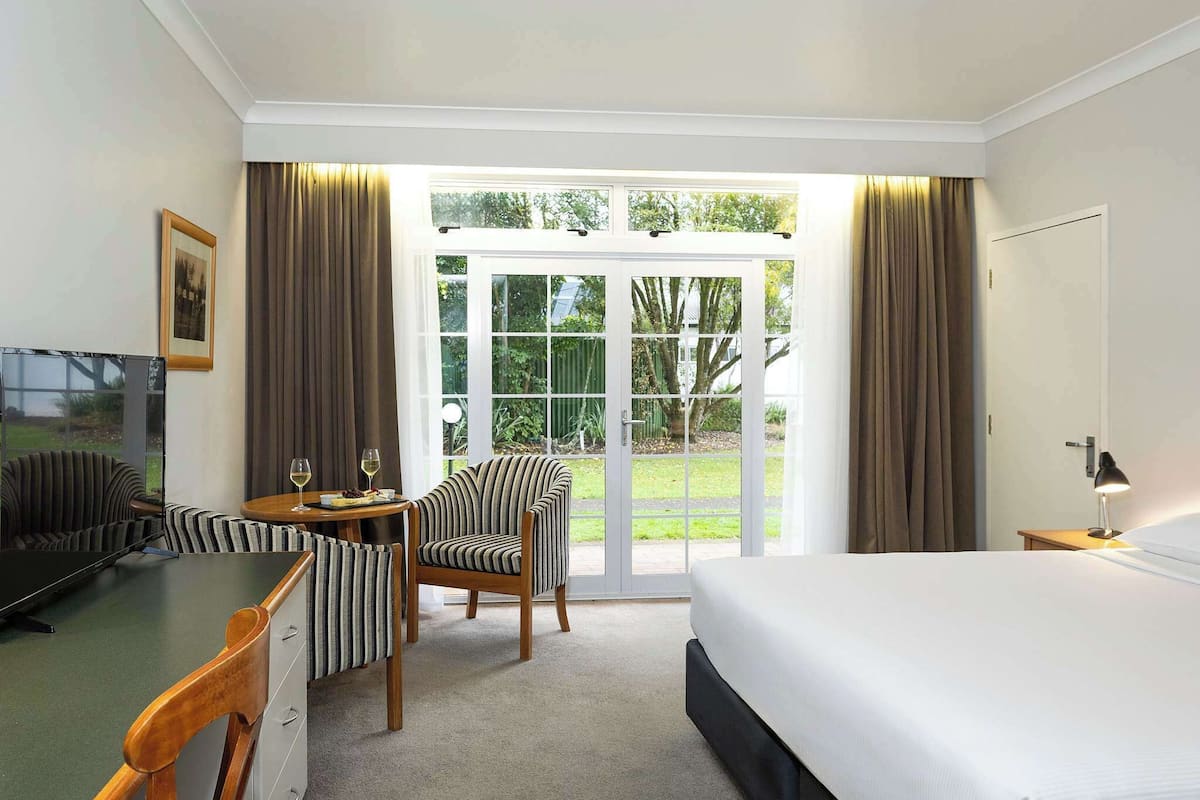 Habitación de hotel con cama, escritorio con silla, televisor y vista al exterior a través de una puerta de cristal.