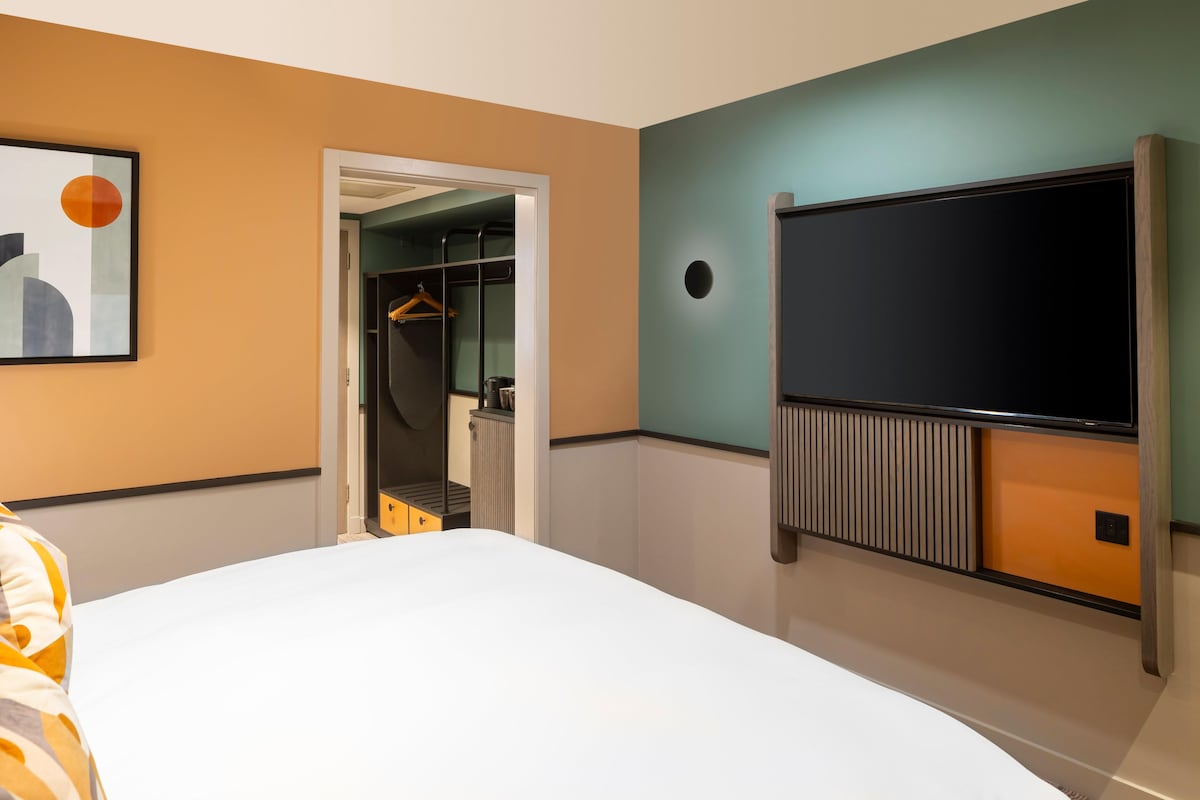 Habitación de hotel con cama, armario, perchero y televisor montado en la pared.