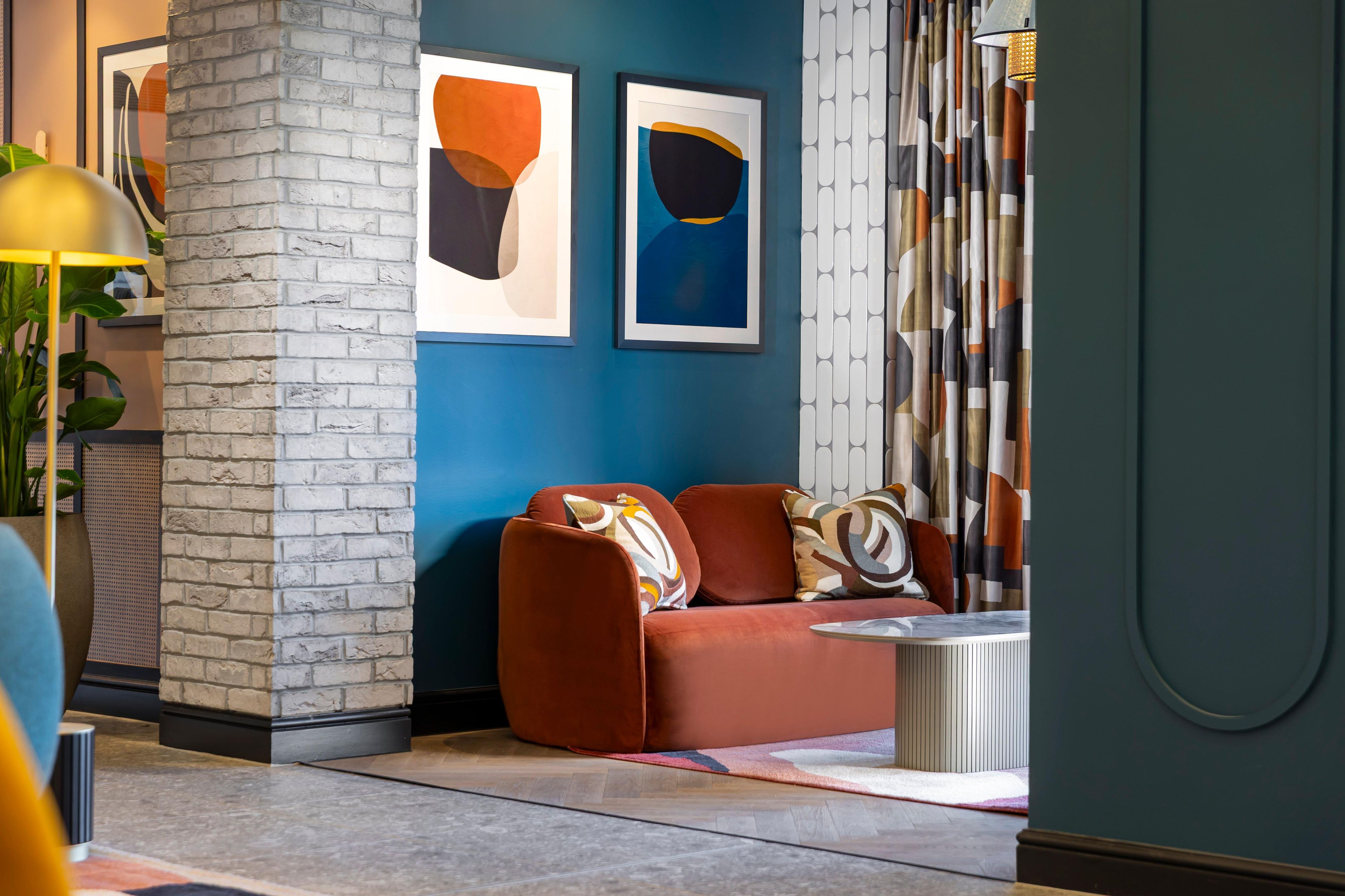A modern interior with a brick accent wall, a red sofa, and abstract art on the wall.
