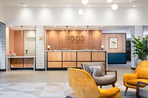 A reception area with a counter, seating, and a wall with a logo. - Voco Fareham-solent (Fareham)