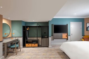 Un dormitorio con una cama, un escritorio con silla, un armario, un televisor montado en la pared y una puerta.