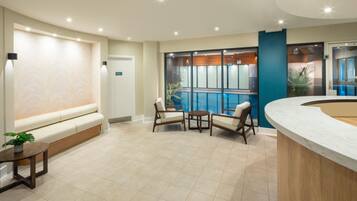 A modern reception area with a seating area, a reception desk, and a view of an indoor pool.