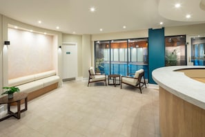 Un área de recepción moderna con zona de estar, mostrador de recepción y vista a una piscina interior.