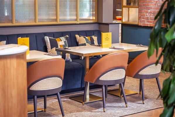 A restaurant with a blue cushioned bench seating, wooden tables, and orange chairs.