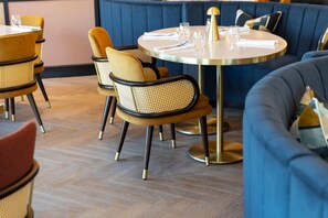 A restaurant interior with round tables, cushioned chairs, and a blue upholstered booth. - Voco Fareham-solent (Fareham)