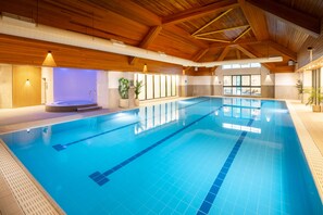 An indoor swimming pool with wooden beams, a hot tub, and potted plants.
