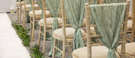Rows of wooden chairs with light green fabric tied at the back, arranged in a line.