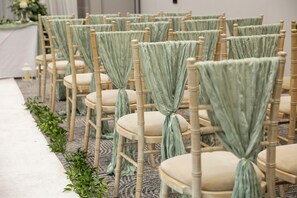 Rows of wooden chairs with light green fabric tied at the back, arranged in a line.