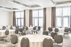 Un salón de conferencias con mesas redondas, sillas y un amplio ventanal con cortinas.