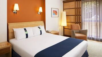 A hotel room with a large bed, two bedside lamps, a chair, a desk, and a window with curtains.