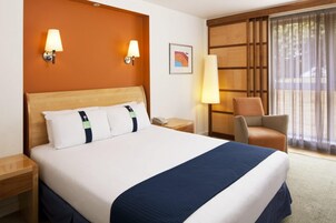 Una habitación de hotel con una cama grande, dos lámparas de noche, una silla, un escritorio y una ventana con cortinas.