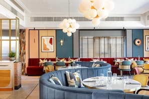 Un restaurante moderno con mesas redondas, asientos tapizados en azul e iluminación decorativa.