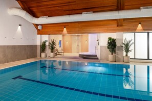 An indoor swimming pool with wooden ceiling beams, potted plants, and a seating area. - Voco Fareham-solent (Fareham)