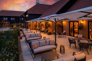 An outdoor patio area with seating arrangements, including sofas and tables, under a covered section with umbrellas. - Voco Fareham-solent (Fareham)