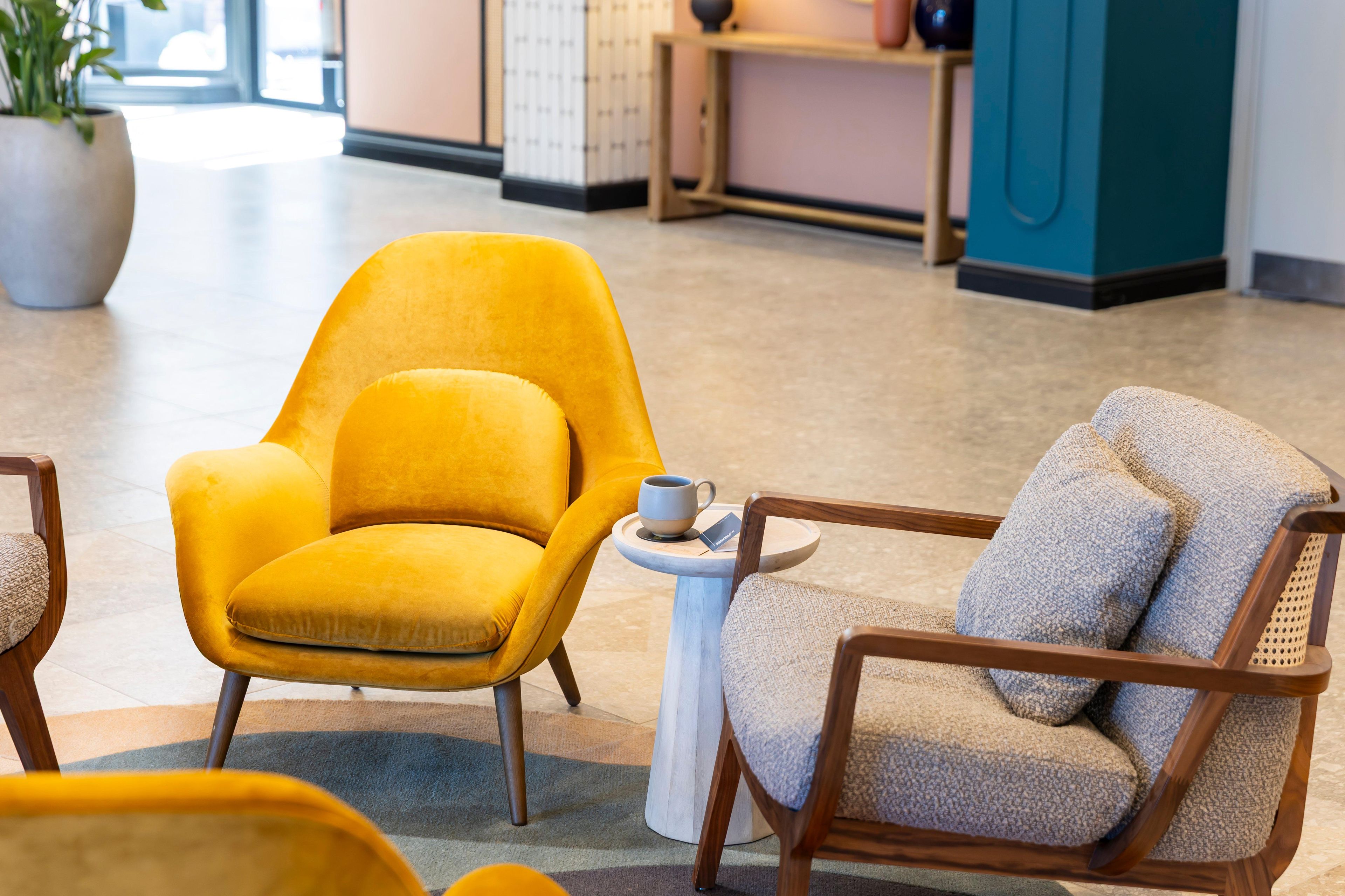 A yellow armchair and a wooden chair with a cushion, both placed on a tiled floor with a small round table between them.