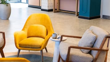 A yellow armchair and a wooden chair with a cushion, both placed on a tiled floor with a small round table between them.