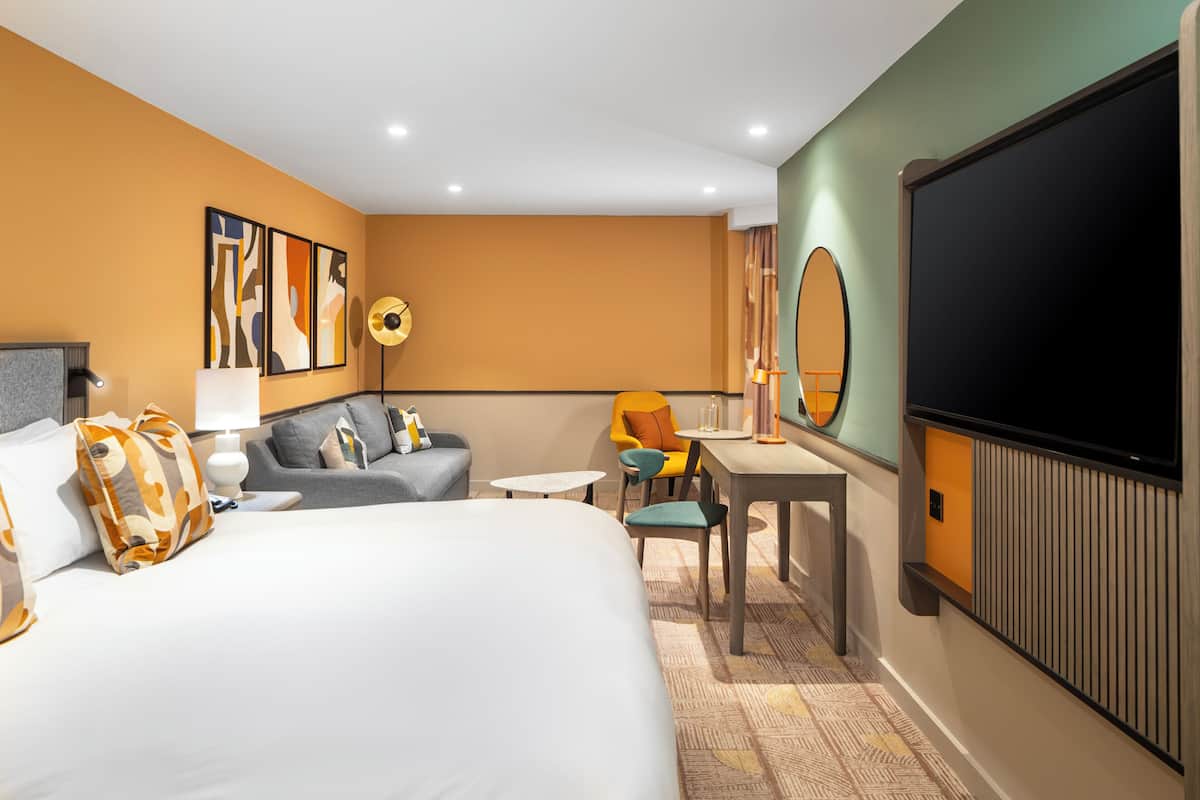 A hotel room with a large bed, a sofa, a desk, and a television.