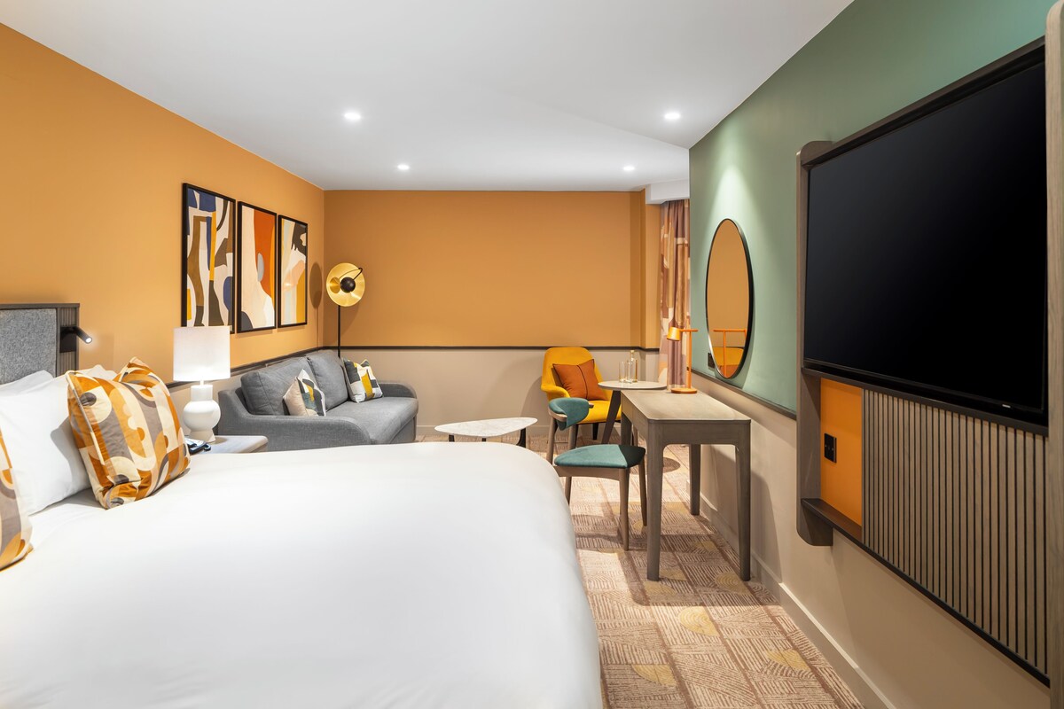 Habitación de hotel con una cama grande, un sofá, un escritorio y un televisor.