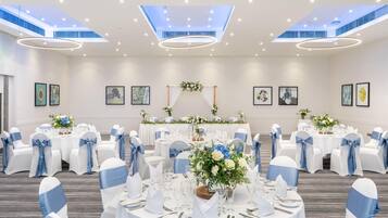 A banquet hall with round tables, white and blue chairs, and ceiling lights.
