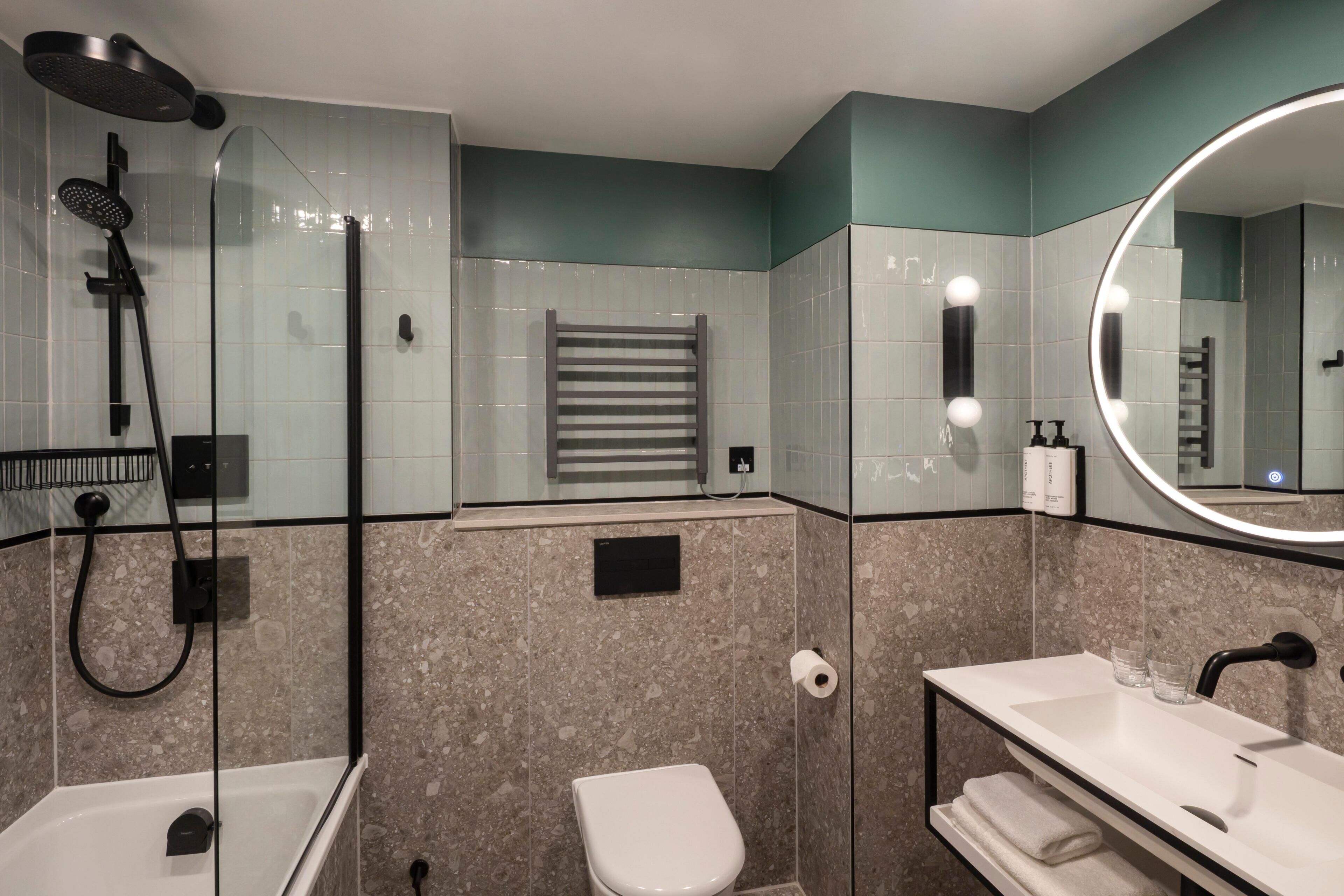 Un baño moderno con ducha envuelta en vidrio, inodoro blanco, tocador con espejo y un perchero para toallas.