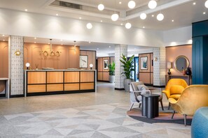 A modern reception area with a wooden reception desk, seating area with chairs, and a large potted plant. - Voco Fareham-solent (Fareham)