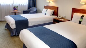 Habitación de hotel con dos camas, una mesita de noche con teléfono y una pequeña mesa con lámpara.