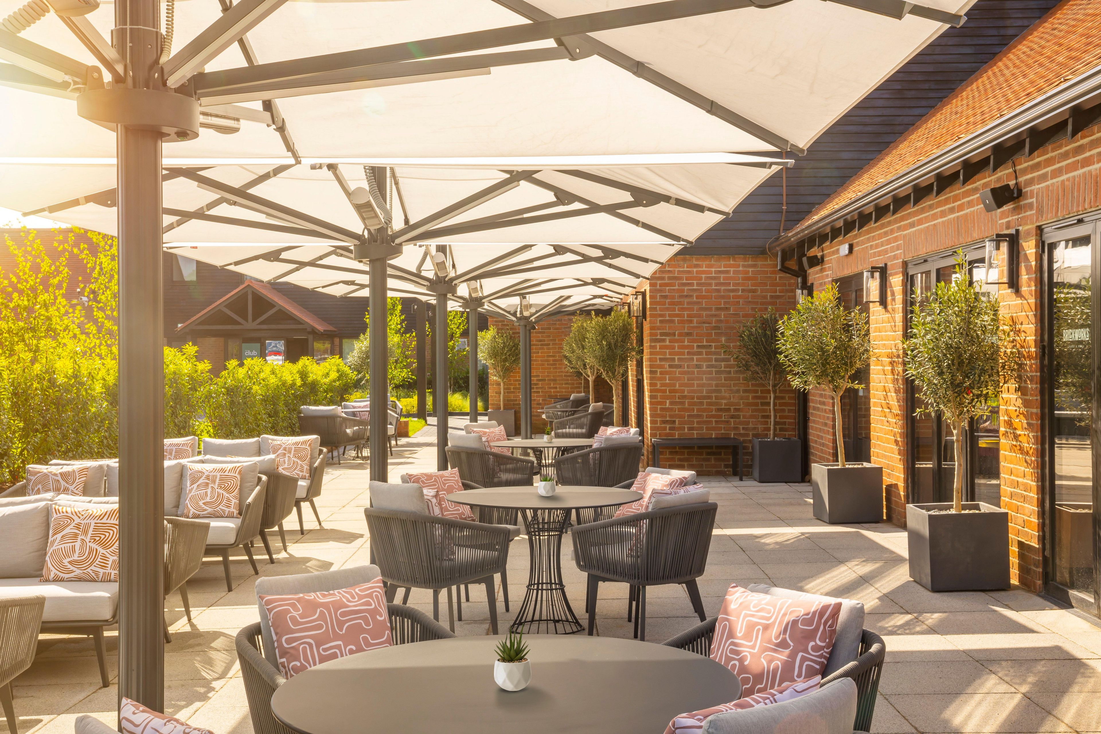 An outdoor patio area with round tables and chairs, a brick building, and potted plants.