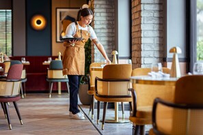 A restaurant interior with wooden tables, wicker chairs, and a waitress serving.
