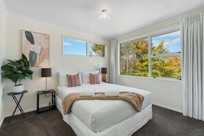 Ein Schlafzimmer mit einem großen Bett, zwei Nachttischen, einer Topfpflanze und einem Fenster mit Vorhängen.