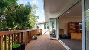 Un terrazzo in legno con vasi di piante, una porta vetrata che dà su una stanza con un divano e un mobile in legno.