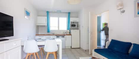 Un soggiorno moderno con un divano blu, una zona pranzo con sedie bianche e una cucina con mobili bianchi e un forno a microonde.