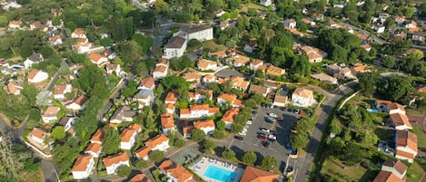 Luchtbeeld van een woongebied met huizen, een zwembad en een strand op de achtergrond.