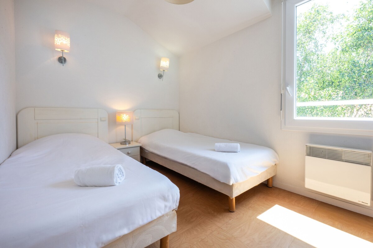 A bedroom with two beds, bedside lamps, a window with a view of trees, and a radiator.