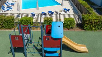 A playground with a slide, climbing structure, and a pool area with lounge chairs.