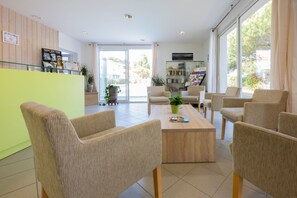 A reception area with a green counter, beige chairs, a wooden coffee table, and a glass door leading outside.